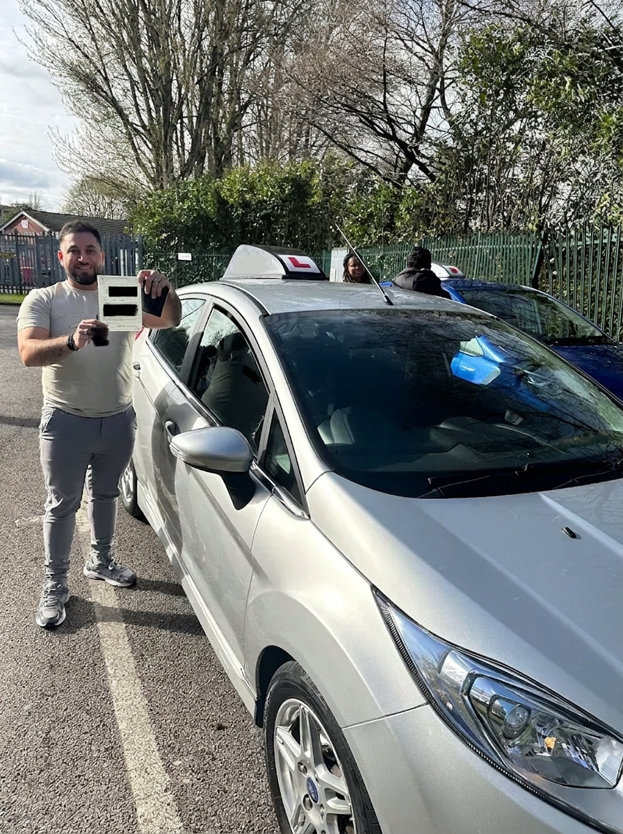 A learner holding their pass certificate by the car