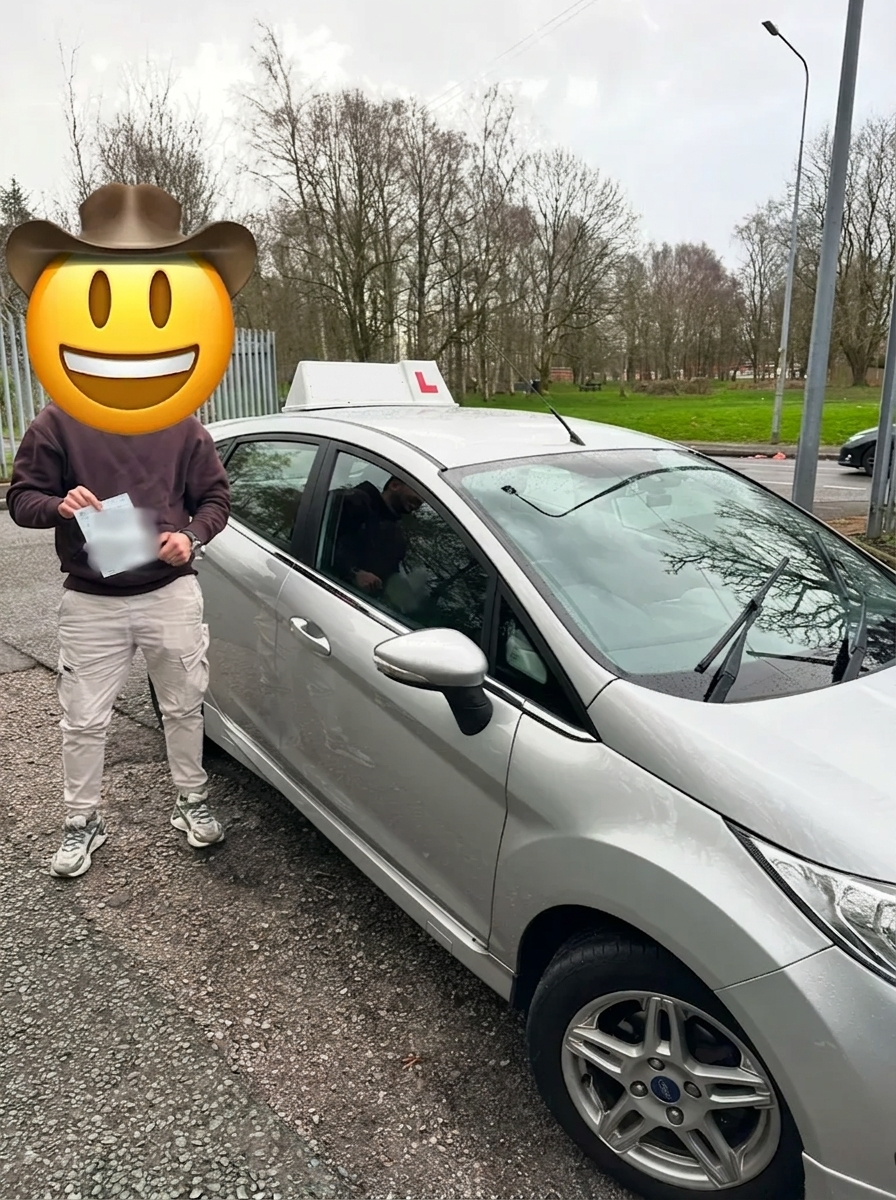 A learner holding their pass certificate beside the car