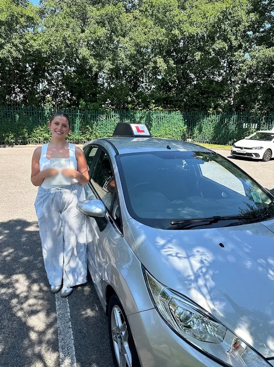 A learner holding their pass certificate beside the car