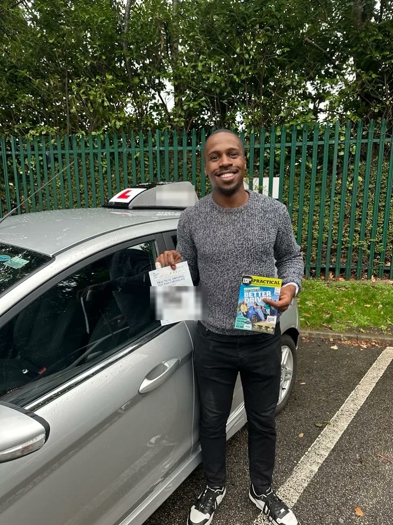 A learner holding their pass certificate beside the car
