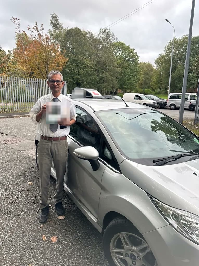 A learner holding their pass certificate by the car