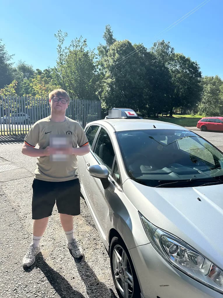 A learner holding their pass certificate beside the car